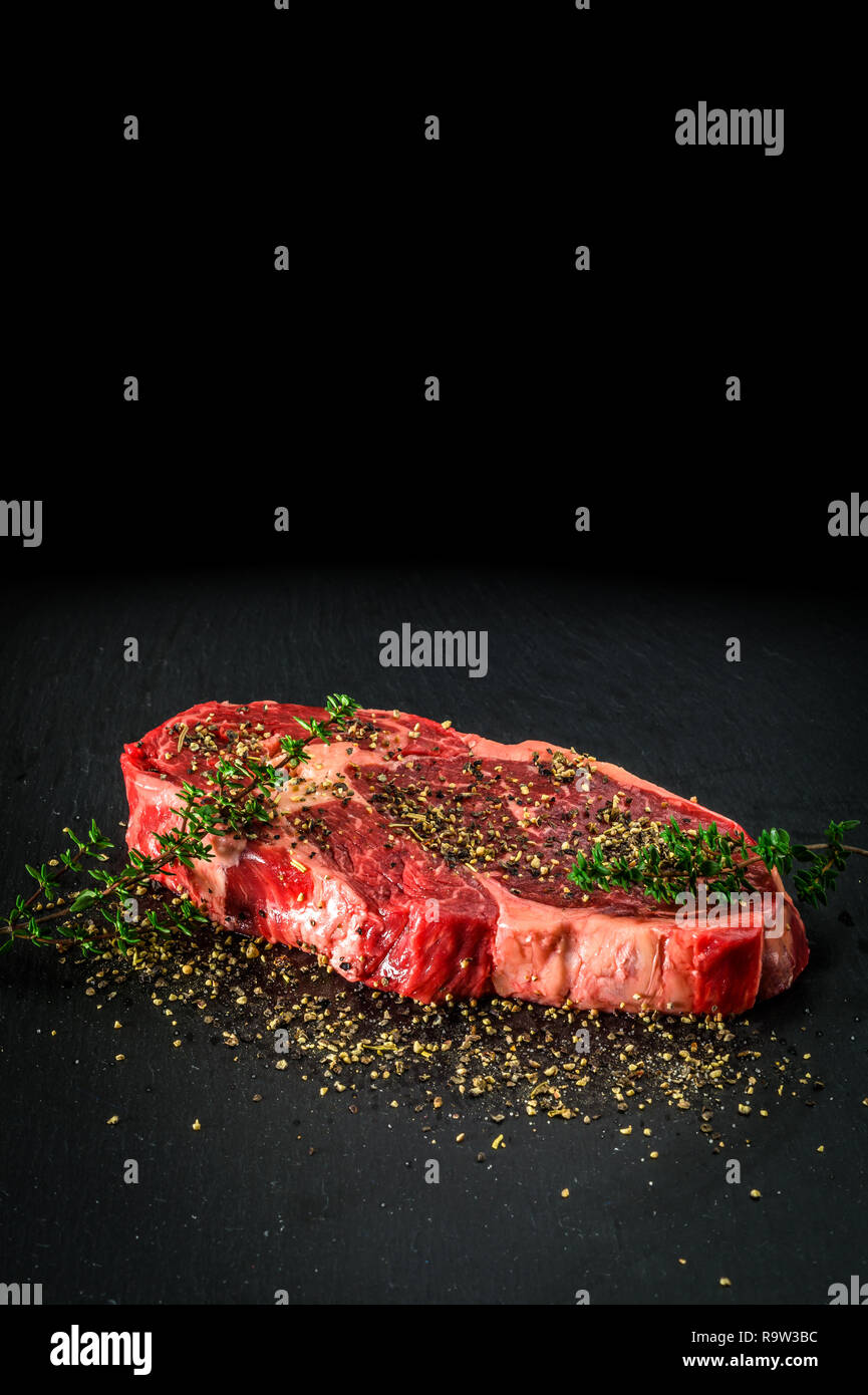 Sec brut de l'entrecôte steak. Barbecure délicieux steak faux-filet avec différentes épices sur une plaque de pierre. Banque D'Images