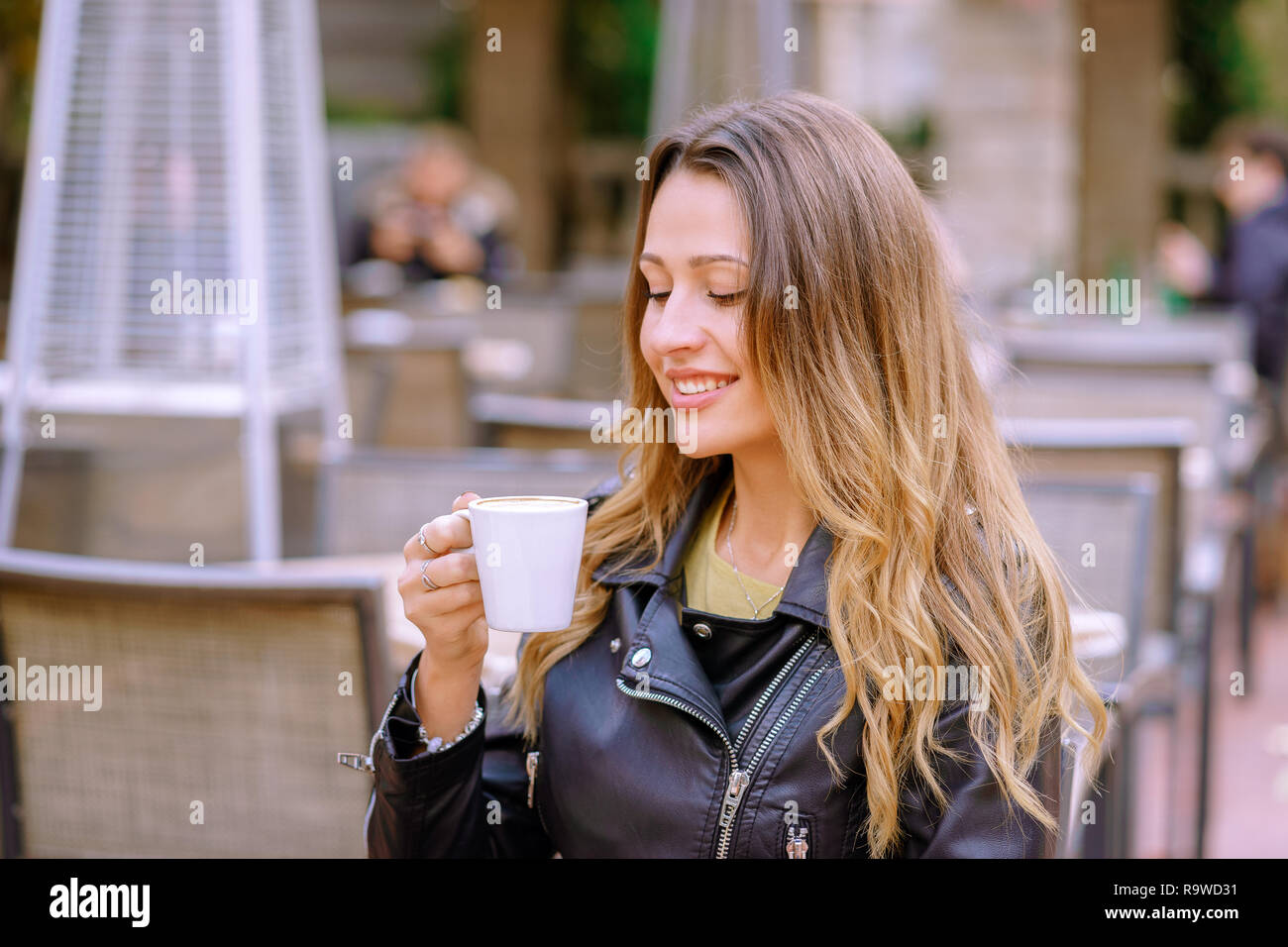 Ambiance happy woman holding une boisson chaude tout en restant assis sur fond flou de outdoor cafe Banque D'Images