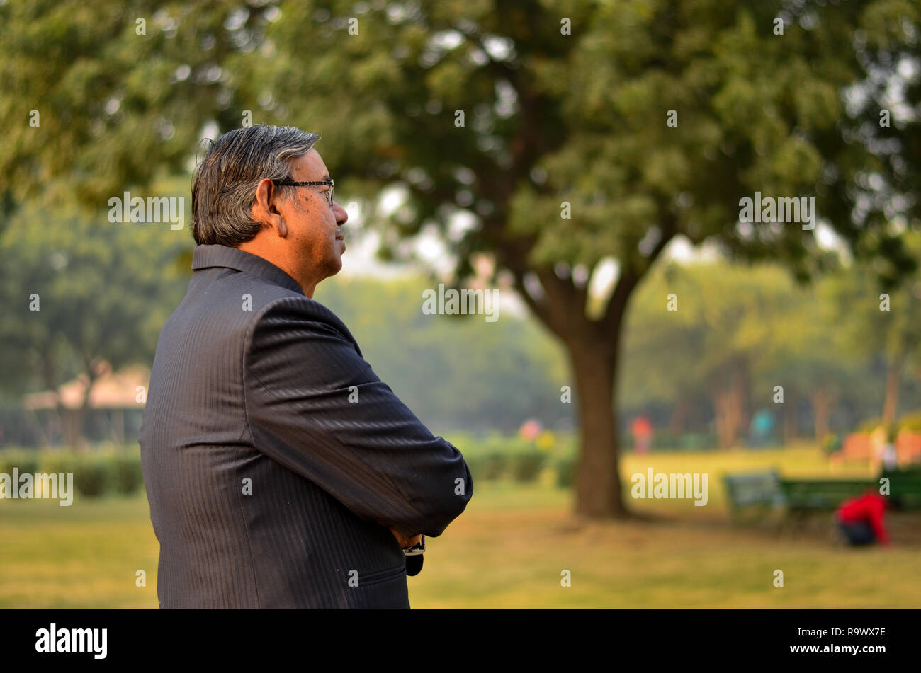 D'un côté indien senior homme portant un costume dans l'extérieur de l'établissement comité permanent et souriant dans un parc à New Delhi, Inde Banque D'Images