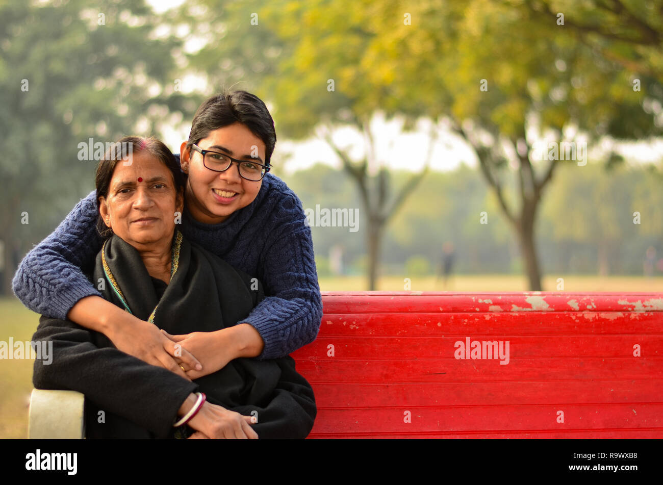 Jeune femme indienne rire avec sa mère qui est assis sur un banc rouge dans un parc à New Delhi, Inde Banque D'Images