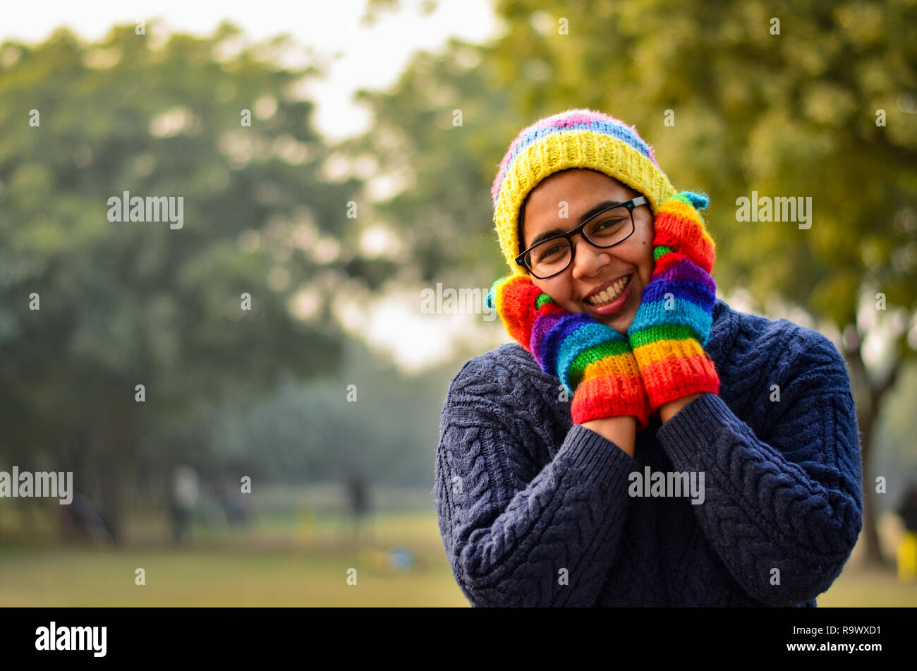 Jeune femme indienne portant bonnet de laine colorés, gants, mitaines et  pull bleu, couvrant son visage avec les mains et souriant dans un parc à  New Delhi, Inde Photo Stock - Alamy