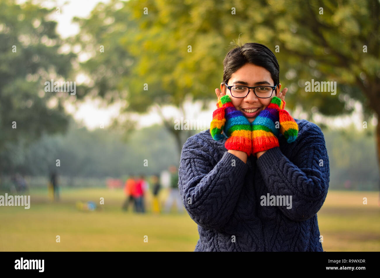 Jeune femme indienne colorée portant des gants, mitaines et pull bleu, couvrant son visage avec les mains dans un parc à New Delhi, Inde Banque D'Images