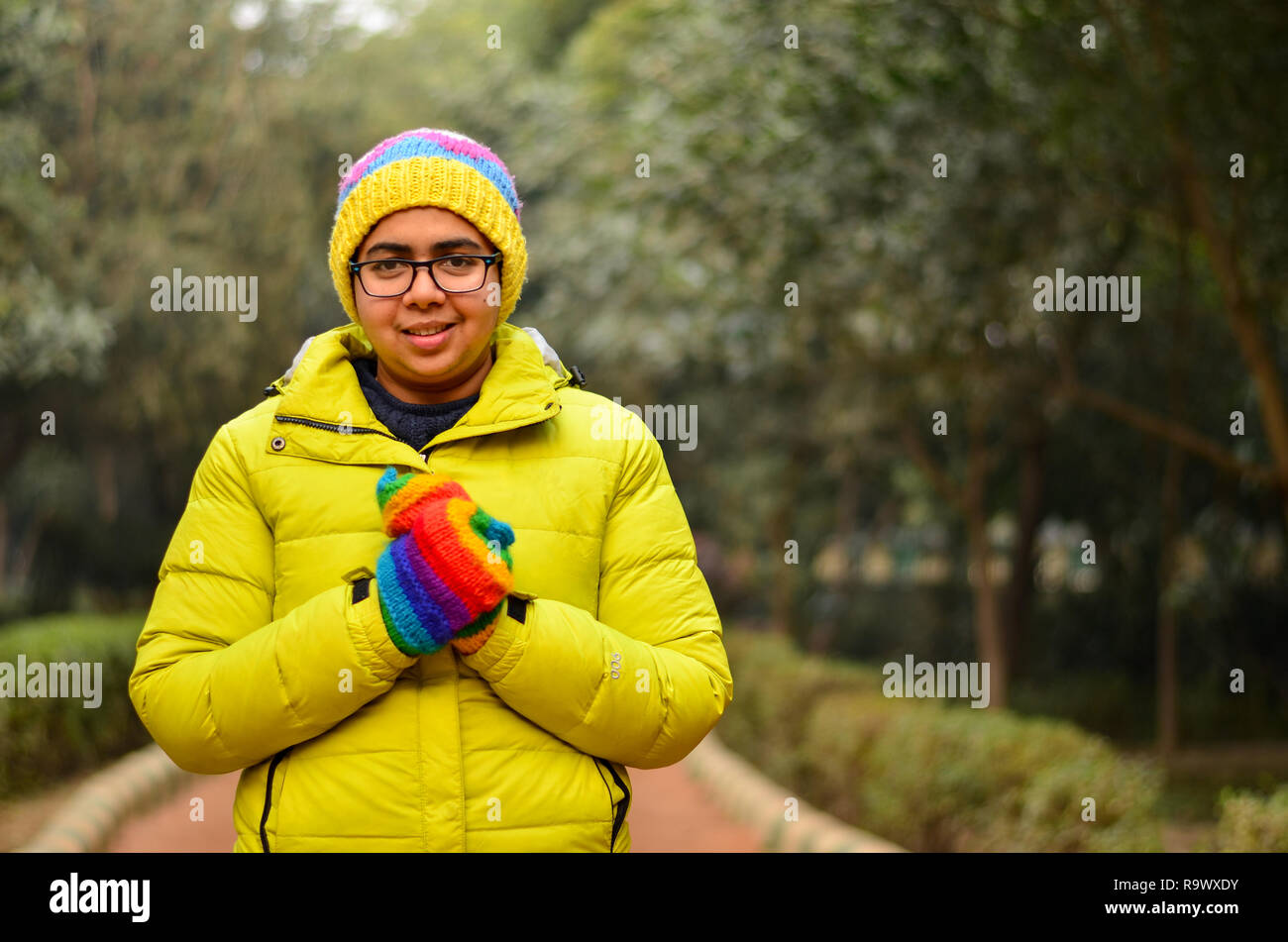 Belle jeune femme indienne portant veste de couleur vert lime et des gants et les comité permanent entre les arbres dans un parc hiverne dans Delhi, Inde Banque D'Images