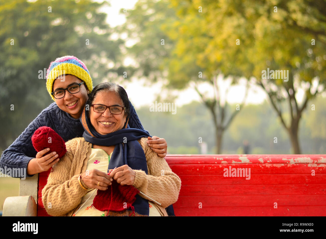 Heureux à la jeune femme indienne avec sa mère knitting sweater qui est assis sur un banc rouge dans un parc à New Delhi, Inde Banque D'Images