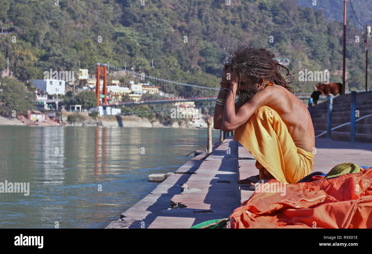 Un jeune Naga Sadhu avec Skinny Corps et Cheveux Dreadlocked assis sur la banque du fleuve saint Ganges à Rishikesh, Uttarakhand, Inde Banque D'Images