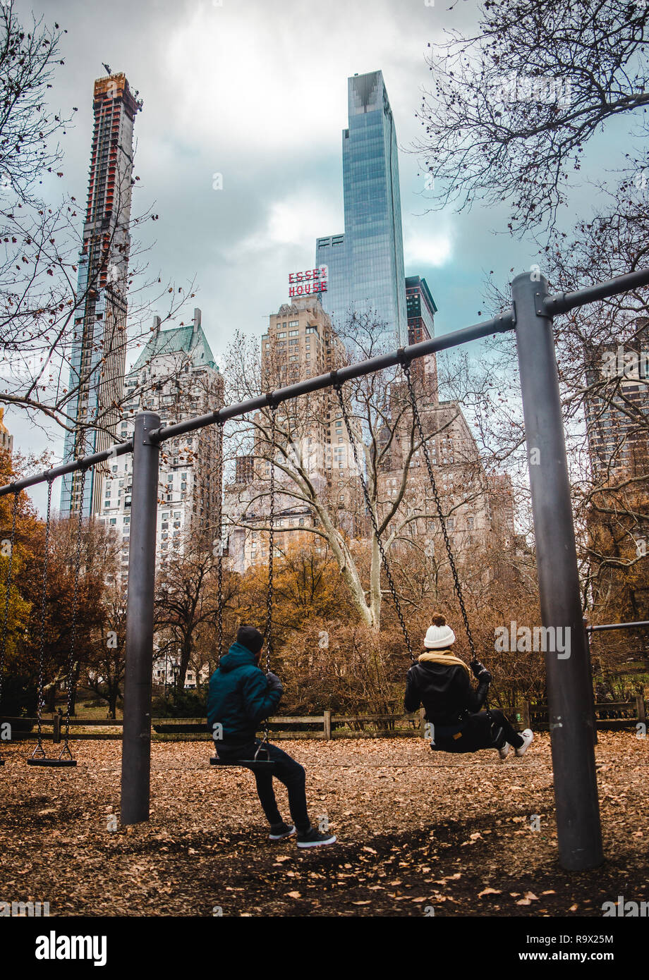 Jeune couple est assis sur des balançoires avec vue sur des gratte-ciel dans Central Park, New York City Banque D'Images