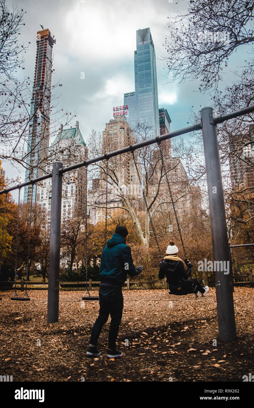 Jeune couple est assis sur des balançoires avec vue sur des gratte-ciel dans Central Park, New York City Banque D'Images