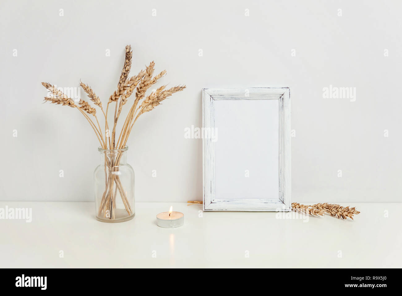 Maquette du châssis vertical avec seigle sauvage bouquet en vase en verre près de mur blanc. Cadre vide maquette pour sa présentation. Pour l'ossature du modèle ar moderne Banque D'Images