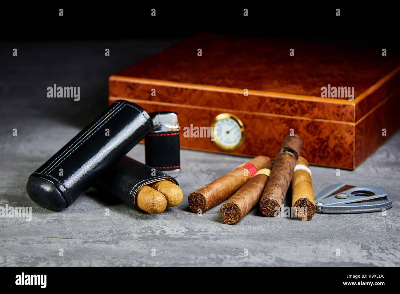 Six cigares cubains sur une table en pierre avec un briquet, cutter et une cave à cigares en bois. Étui en cuir. Banque D'Images