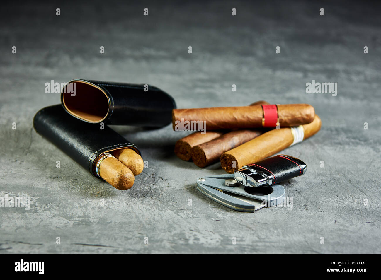 Six cigares cubains sur une table en pierre avec un briquet, cutter et un étui en cuir. Banque D'Images