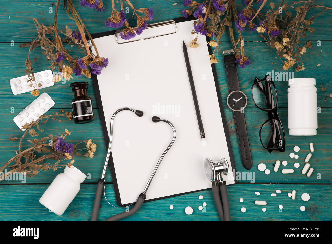 Lieu de travail de médecin - médecine stéthoscope, presse-papiers, bouteille, fleur, lunettes, regarder et pils sur bureau en bois Banque D'Images