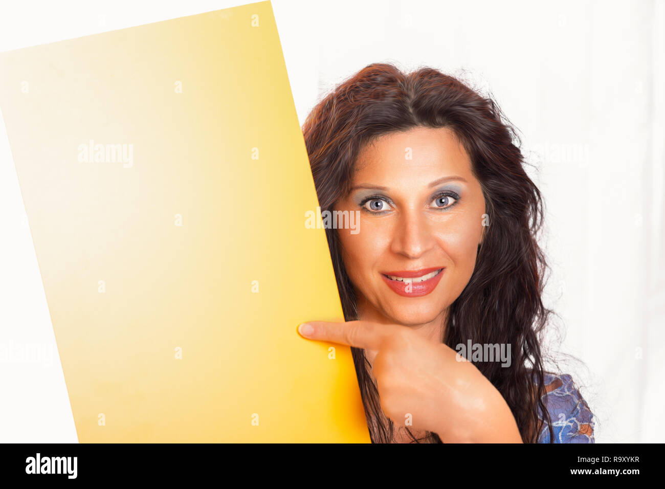 Fille de l'Europe du Nord avec des yeux d'un bleu profond pointant son doigt jaune vide pancarte en orientation portrait Banque D'Images
