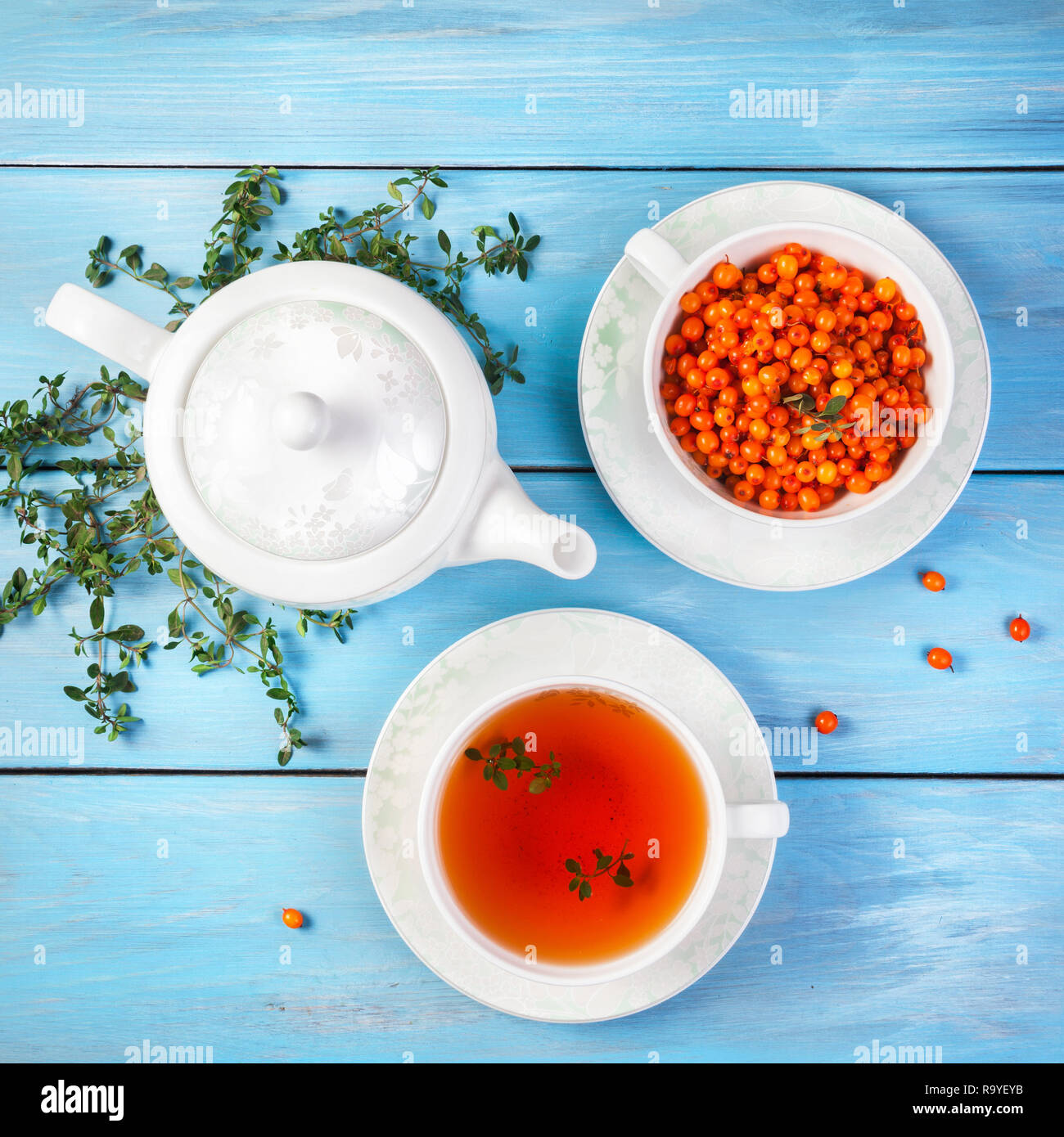 Thé de fines herbes et de baies dans la tasse près de la théière et les feuilles de thym on blue background Banque D'Images