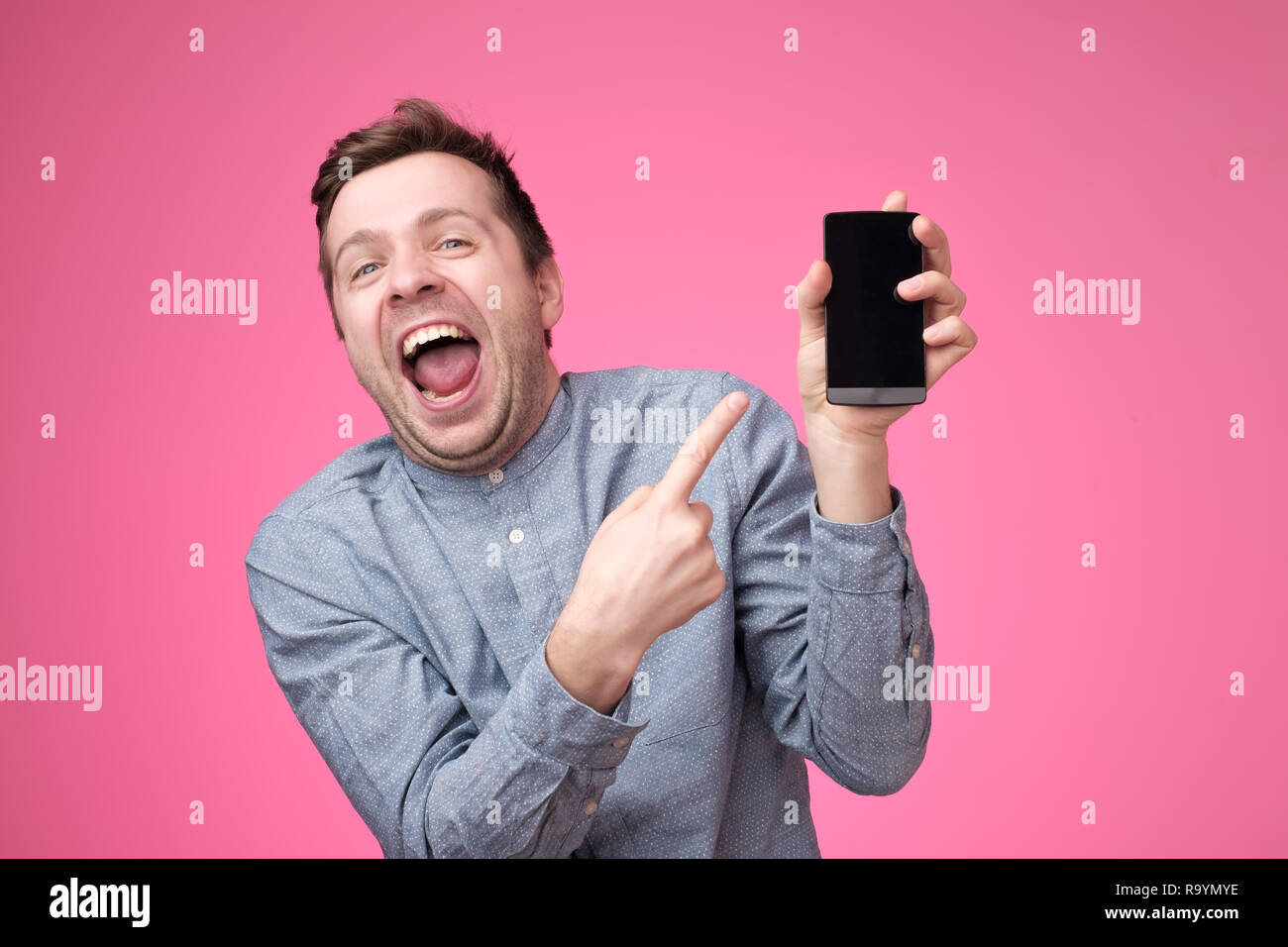 Handsome young man holding smartphone, montrant à l'appareil photo gadget, isolé sur fond rose. Banque D'Images