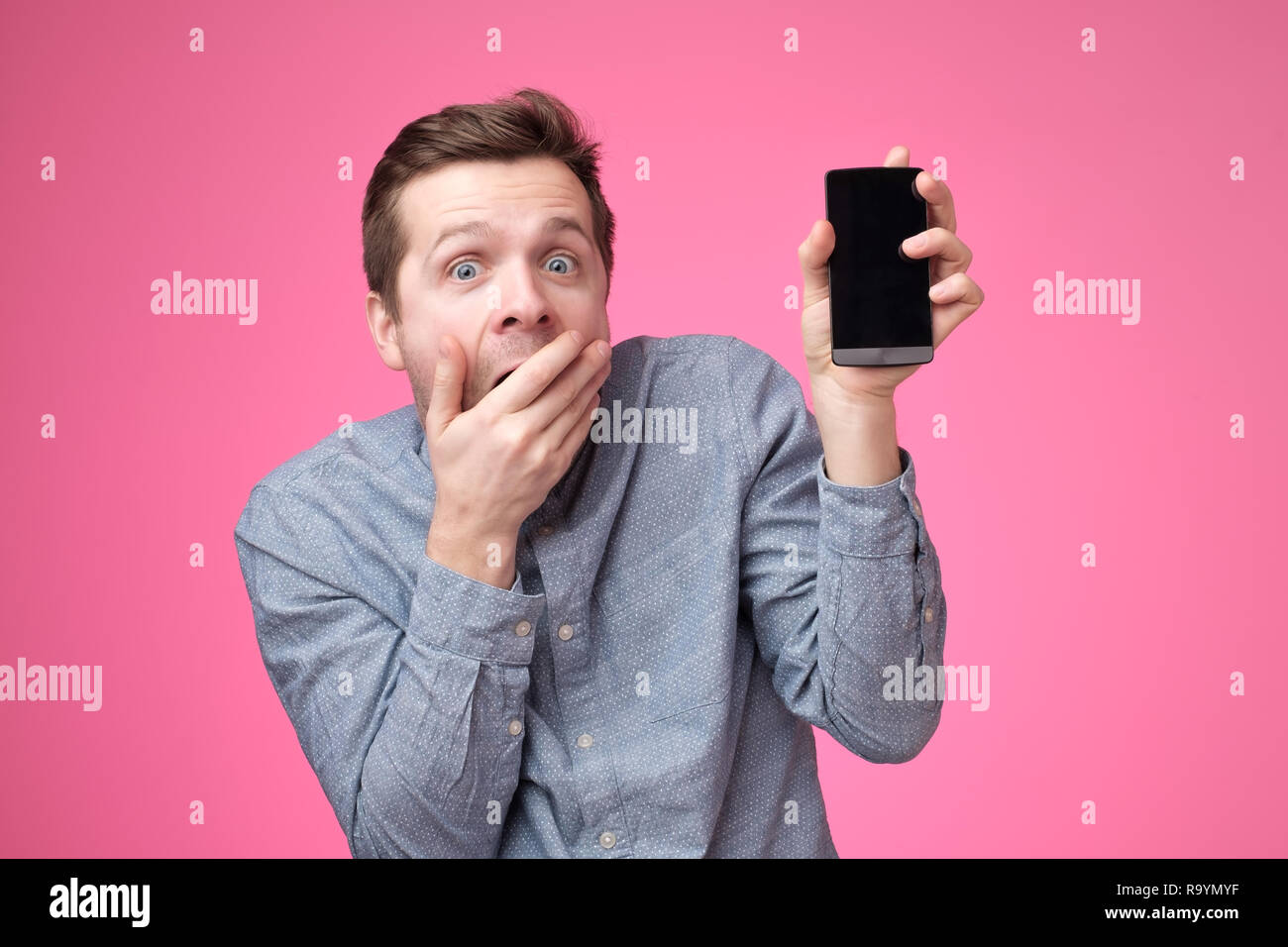 Handsome young man holding smartphone, montrant à l'appareil photo gadget, isolé sur fond rose. Banque D'Images