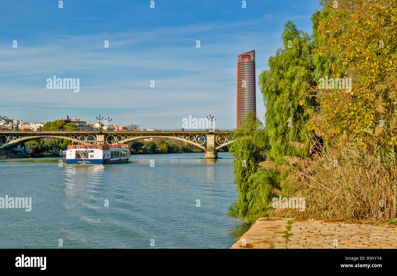 Espagne Séville Séville OU LA TOUR CAJASOL AVEC BATEAU DE TOURISME SUR LA RIVIÈRE GUADALQUIVIR, qui passe sous le pont en arc métallique de Triana Banque D'Images