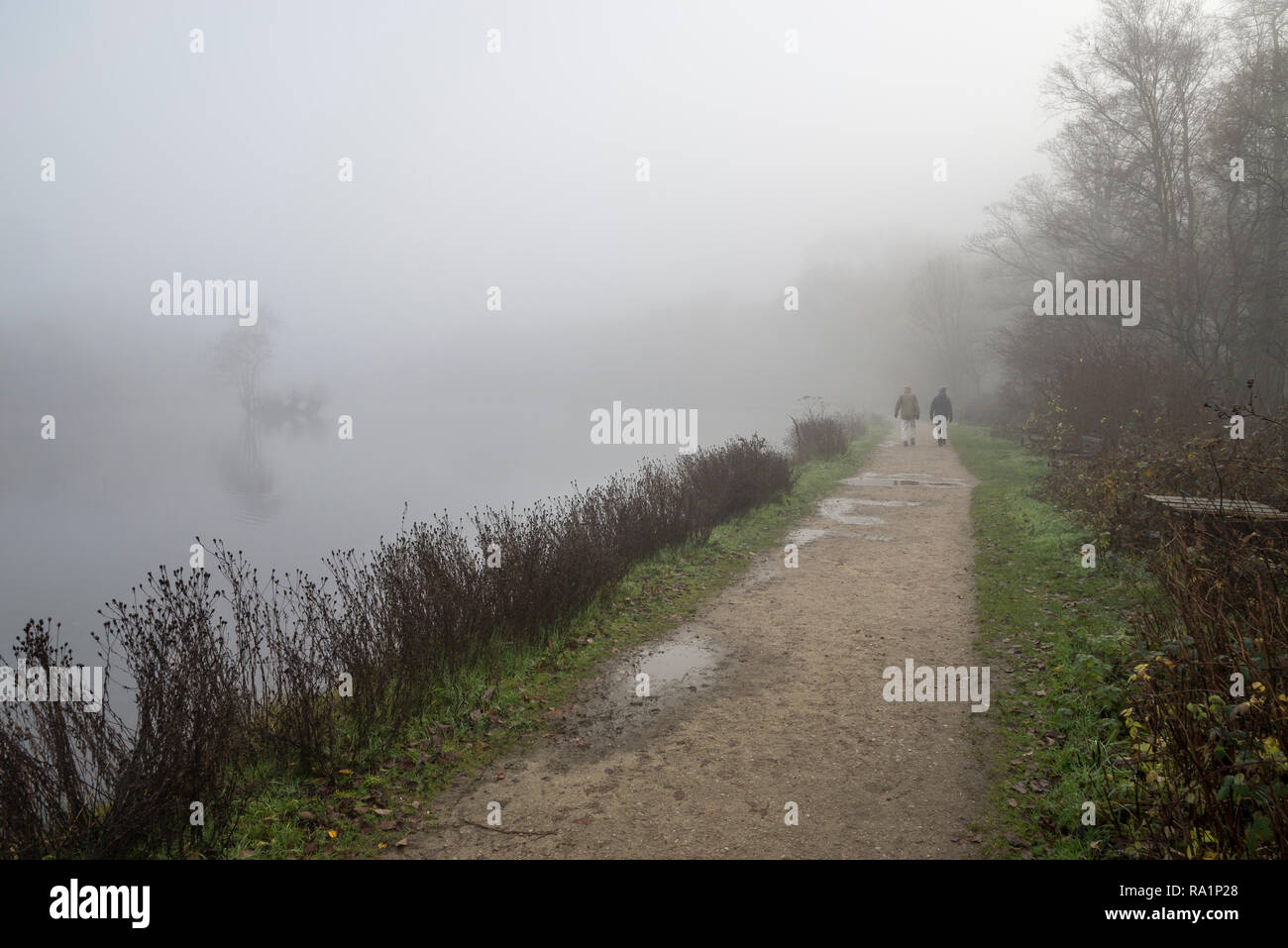 Deux hommes marchant à côté du lac à Etherow country park sur un matin d'hiver brumeux, Compstall, Stockport, Angleterre. Banque D'Images