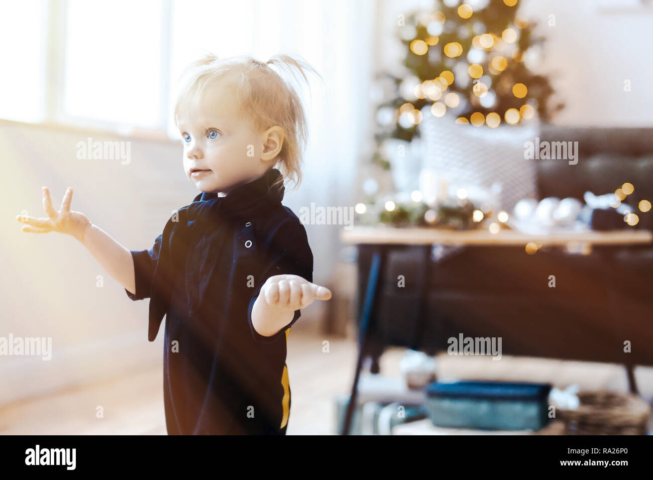 Cute toddler girl surpris dans la salle de séjour. Arbre de Noël est sur l'arrière-plan. Banque D'Images