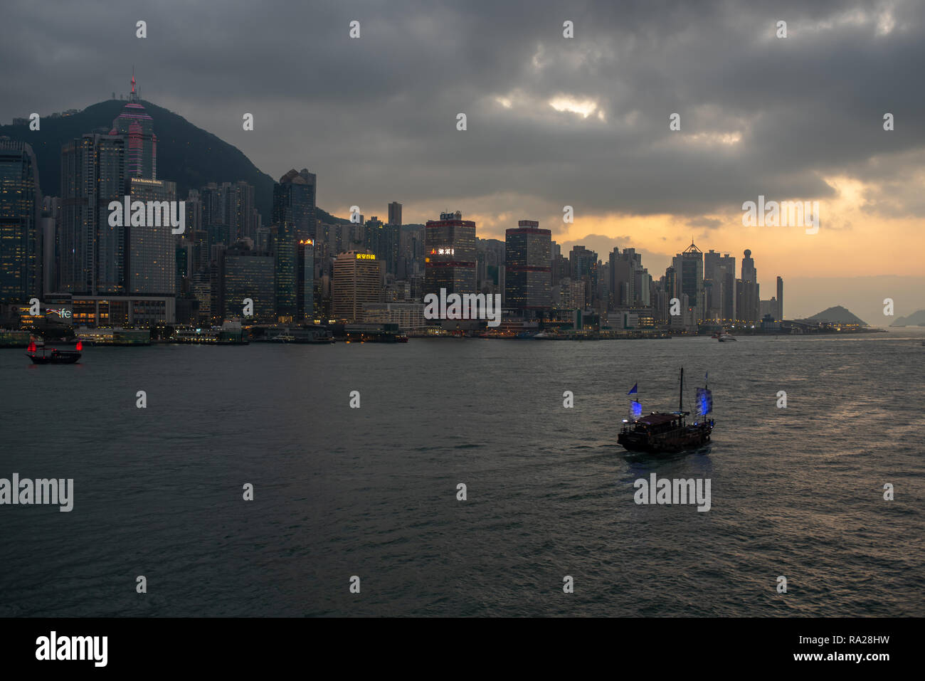 Les jonques touristiques bien éclairé dans le port de Victoria sous la toile de gratte-ciel scintillants, alors que le soleil se couche sur Kennedy Town, Hong Kong Banque D'Images