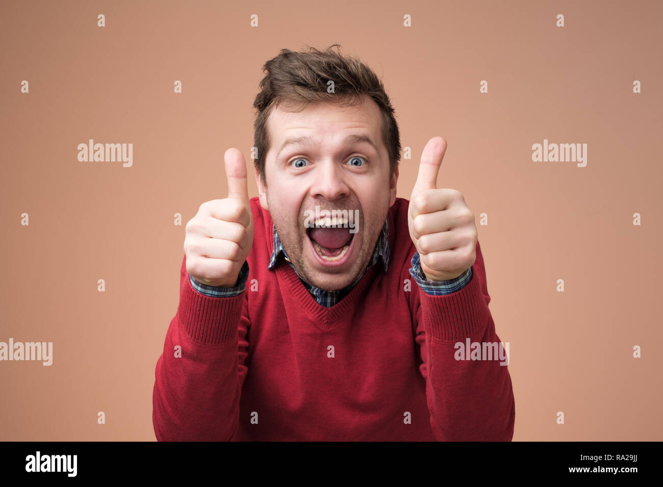 Heureux bel homme en pull rouge showing Thumbs up Banque D'Images