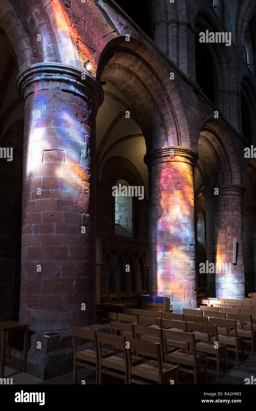 Arches de l'intérieur de la cathédrale St Magnus à Kirkwall sont éclairés par un arc-en-ciel de lumière à travers les vitraux de la façade ouest Banque D'Images