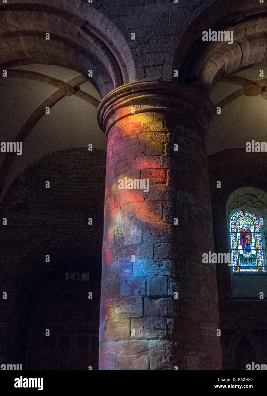 Arches de l'intérieur de la cathédrale St Magnus à Kirkwall sont éclairés par un arc-en-ciel de lumière à travers les vitraux de la façade ouest Banque D'Images