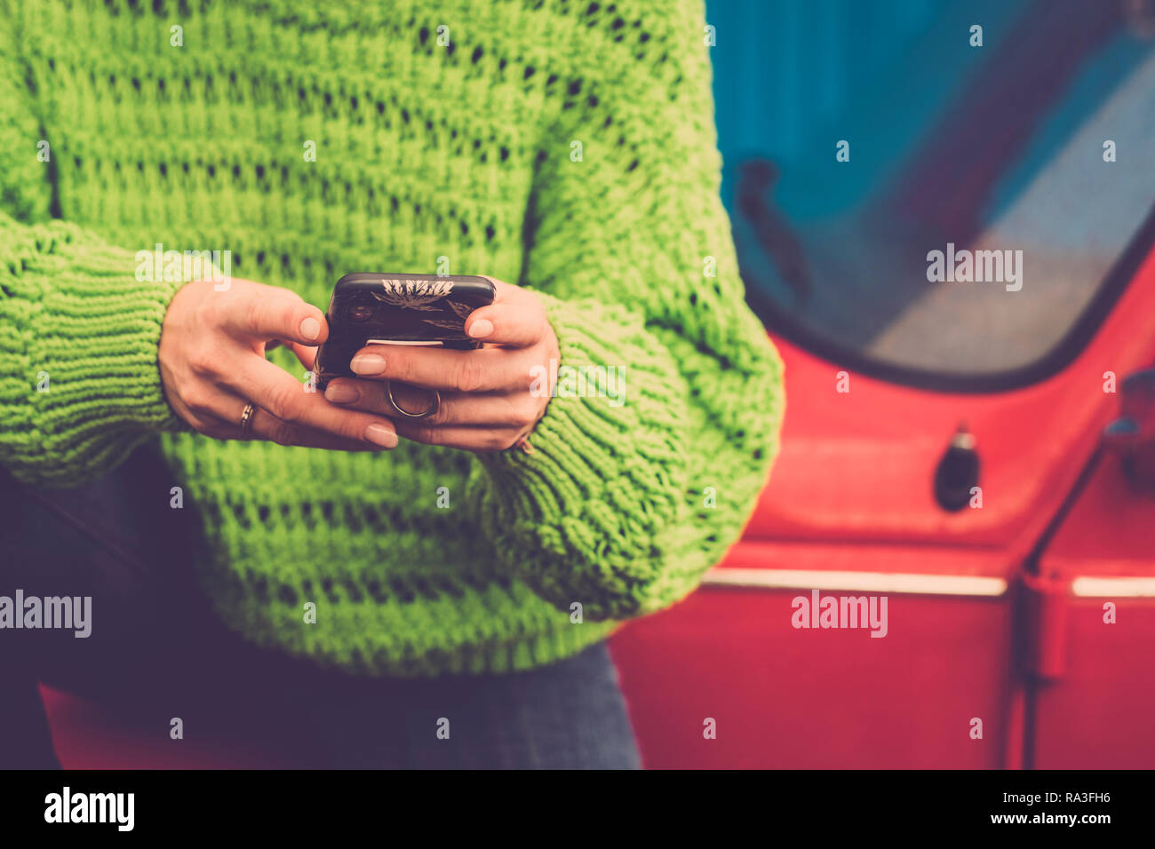 Close-up female hands en utilisant la messagerie instantanée et à la technologie moderne smart phone - vestes vert et rouge old vintage car en arrière-plan - de couleur lifestyl Banque D'Images