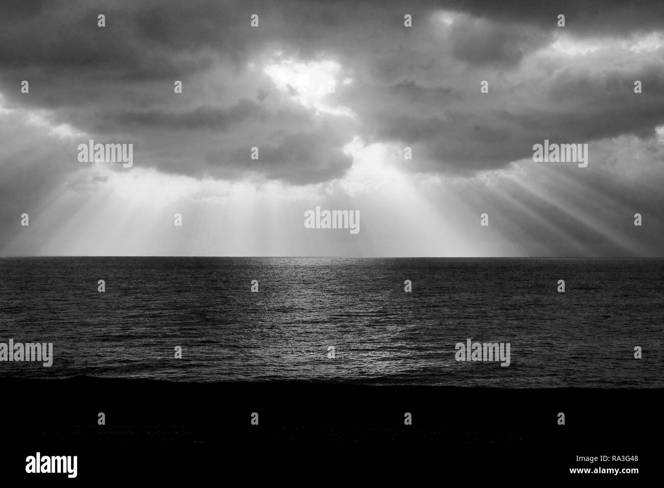 Photographie en noir et blanc d'un grand nombre de longues poutres de la lumière du soleil qui brillait à travers les nuages spectaculaires longue coulée des rayons de lumière sur la mer de la mer gl Banque D'Images