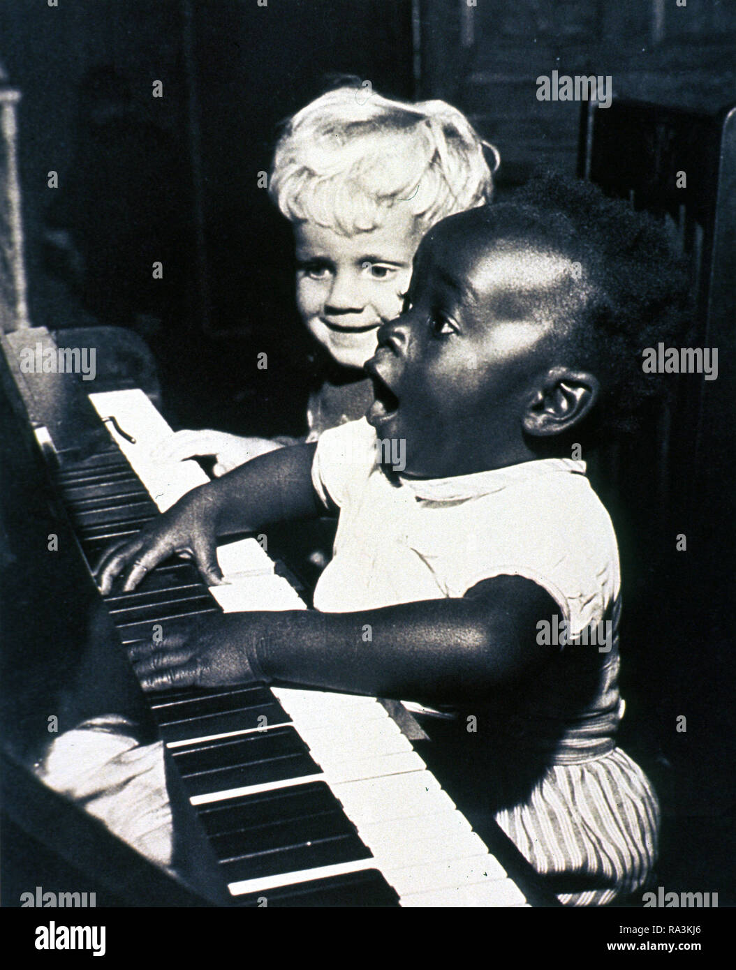 Deux enfants sont assis à un piano. L'African American enfant joue du piano et chante comme l'autre enfant regarde sur ca. Années 1950 Banque D'Images