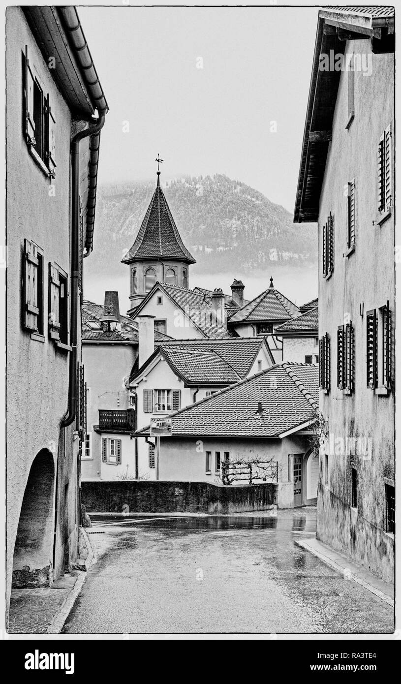 Village alpin idyllique en Suisse avec un vlilage route menant au bâtiment ancien et de nombreux toits en arrière-plan en noir et blanc Banque D'Images