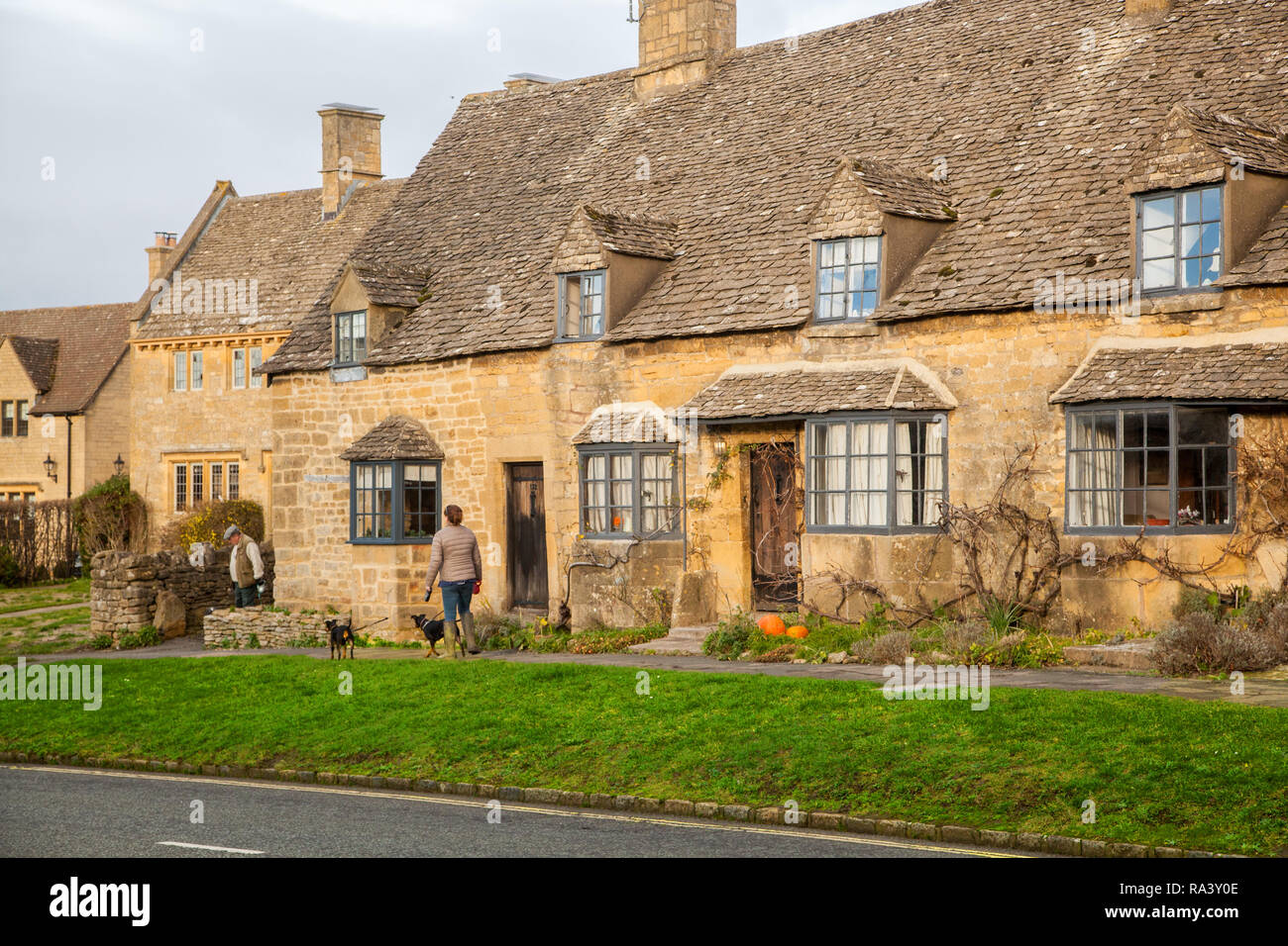 Femme marche ses chiens à travers la pittoresque village de Cotswold quintessenciel de Broadway avec ses bâtiments et maisons en pierre de Cotswold Banque D'Images