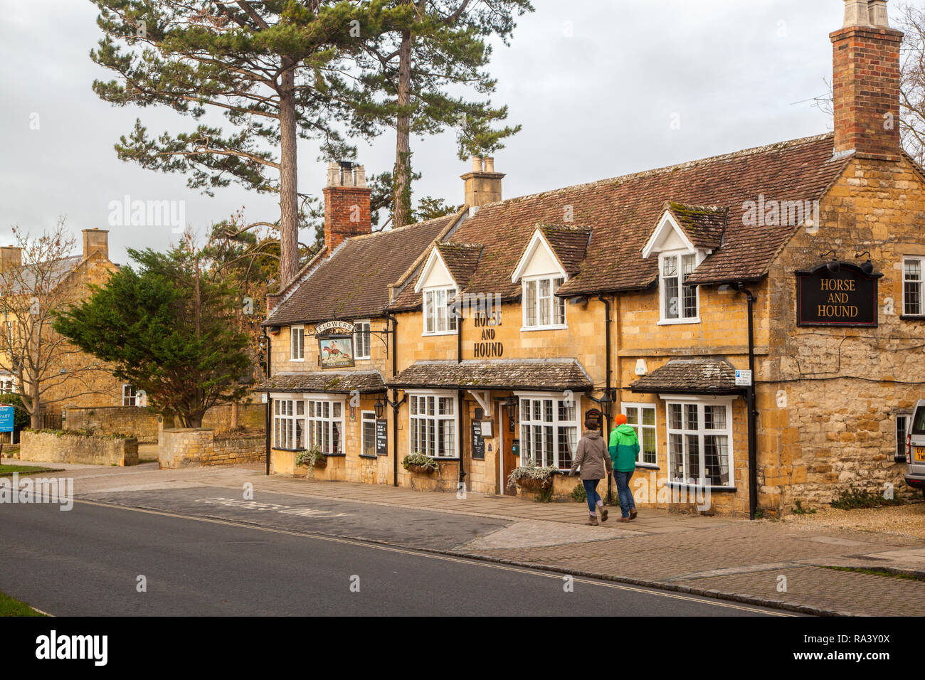 L'homme et la femme devant le Cheval et Hound pub / Inn dans le pittoresque village de Cotswold de Broadway avec ses bâtiments et maisons en pierre de Cotswold Banque D'Images