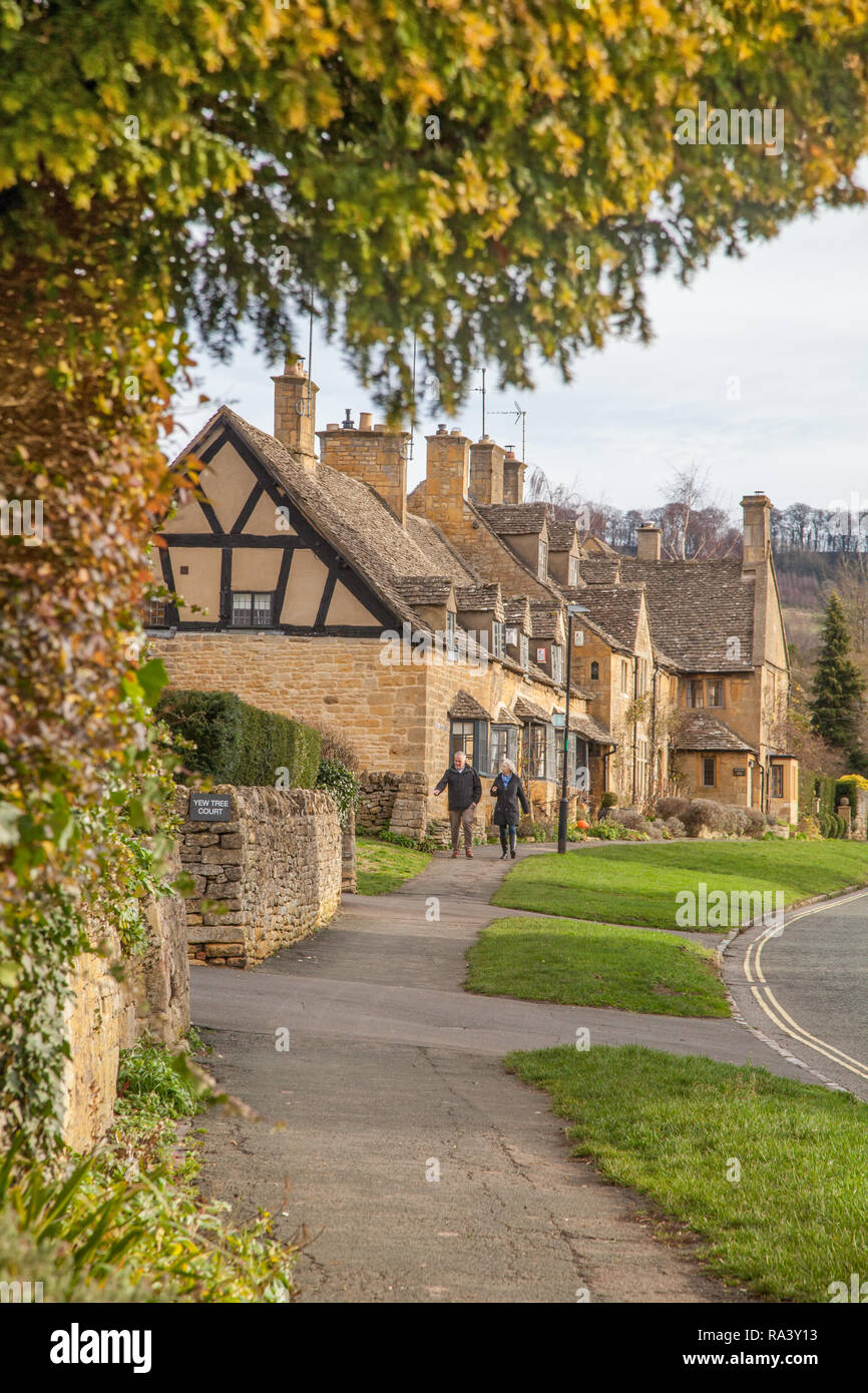 L'homme et de la femme marchant à travers le pittoresque village de Cotswold quintessenciel de Broadway avec ses bâtiments et maisons en pierre de Cotswold Banque D'Images
