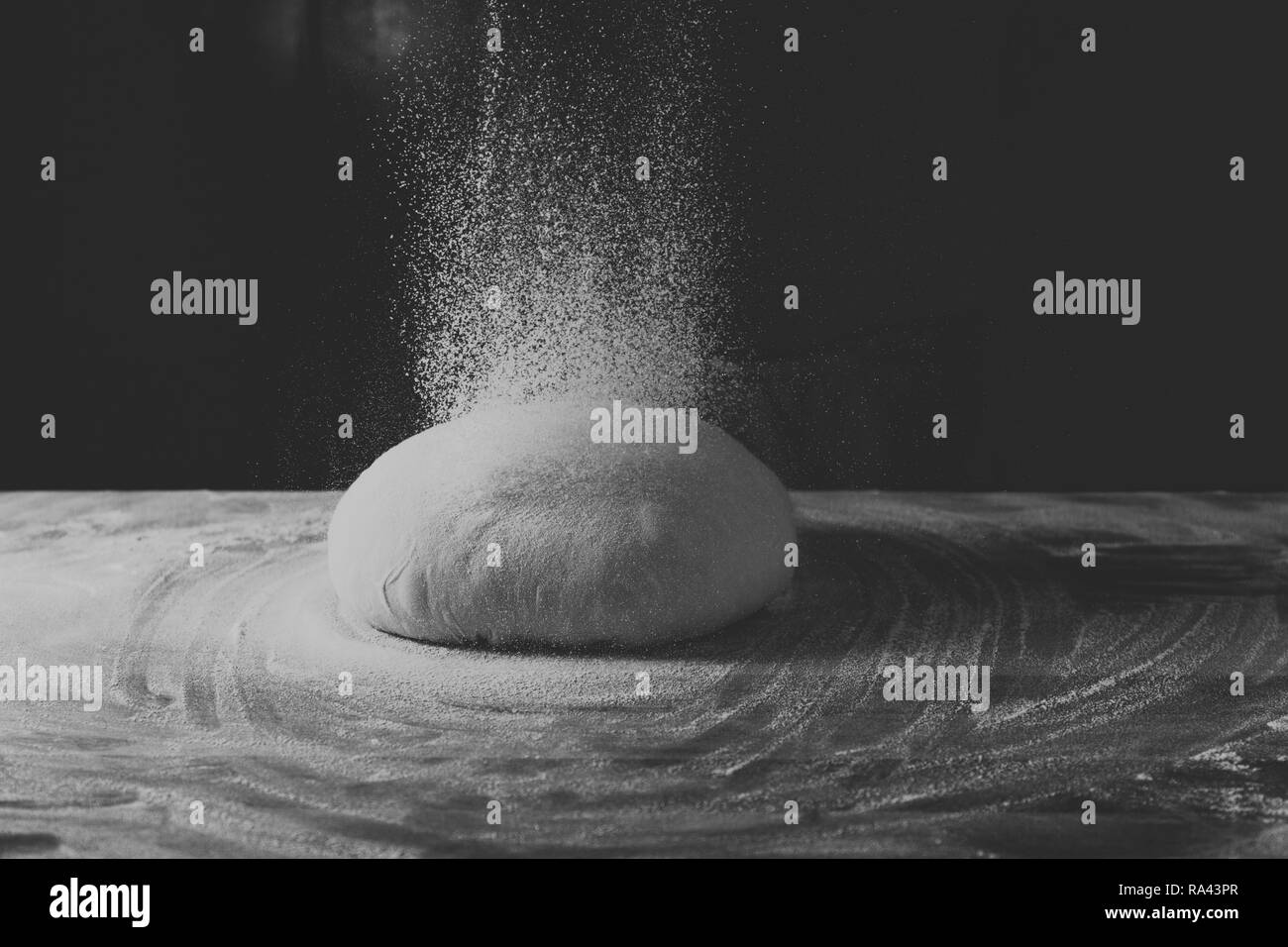 La pâte en forme de bol se trouve sur une table de cuisson en bois sombre sur un fond noir. Saupoudrée de farine. Vue de côté, photo horizontale Banque D'Images