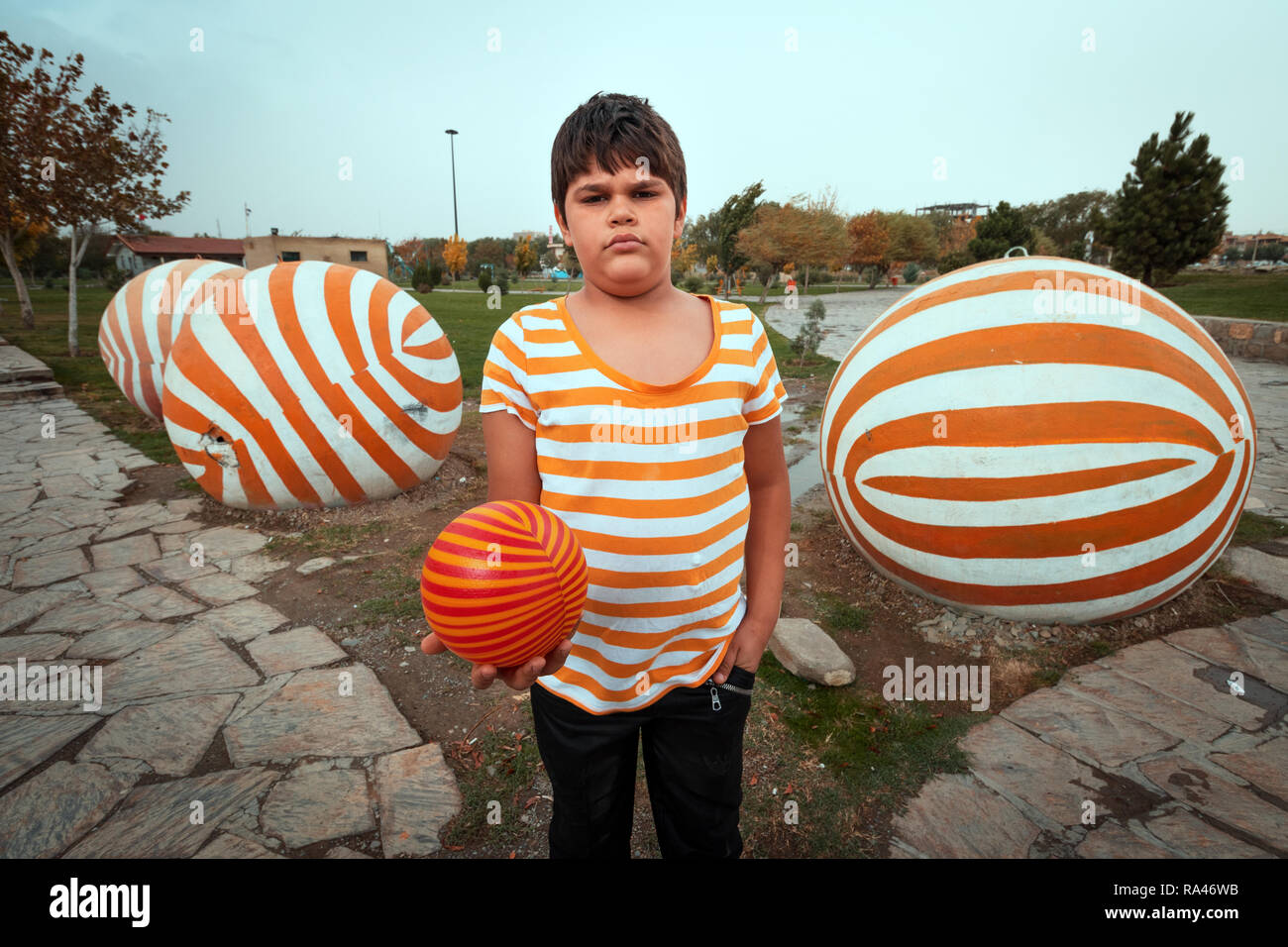 Un adolescent portant un t-shirt à rayures orange avec une balle sur sa main Banque D'Images Un adolescent portant un t-shirt à rayures orange avec une balle sur sa main Banque D'Images