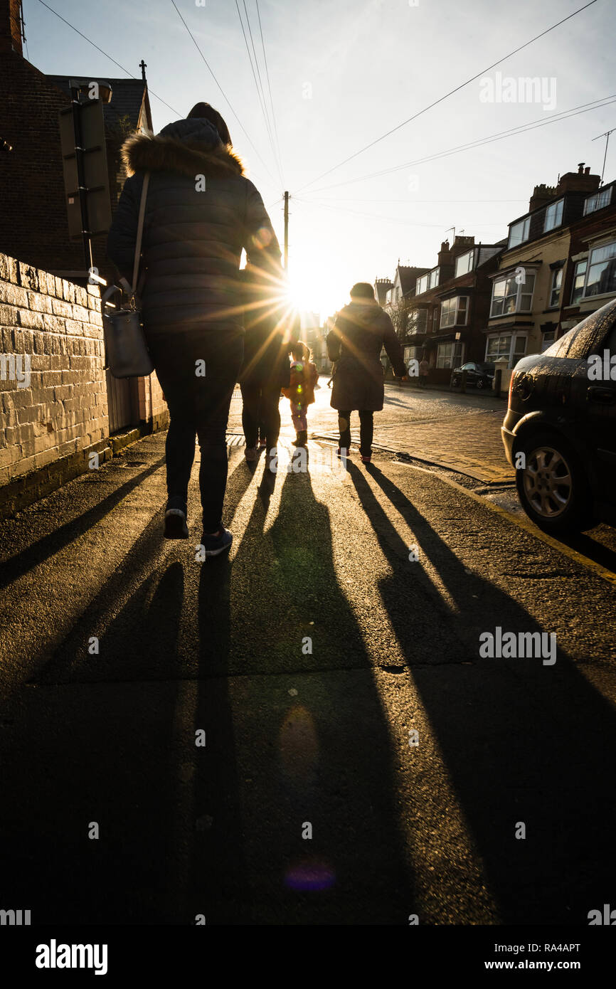 Balades en famille dans la rue dans une ville balnéaire britannique vers la lumière du soleil Banque D'Images