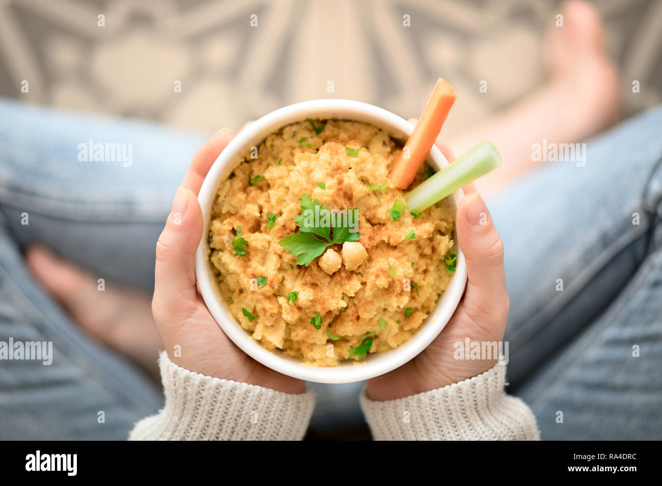 Pieds nus Femme tenant un bol d'hummus, carotte et céleri assis sur le plancher Banque D'Images