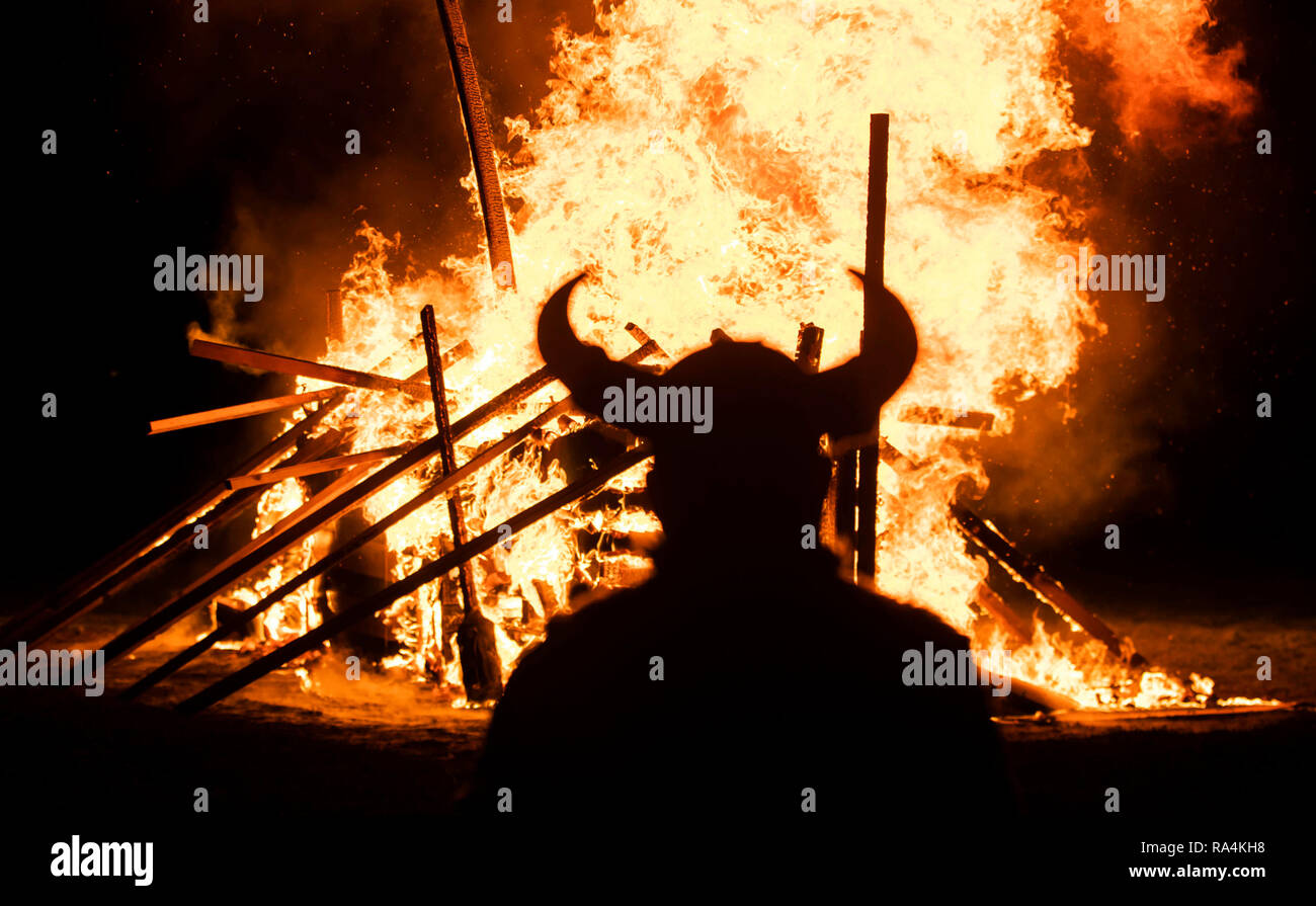 Une personne en costume Viking en face d'un bateau viking brûlant pendant la fête du Feu, Flamborough Viking un défilé à thème, le Nouvel An, à Flamborough près de Bridlington, Yorkshire, au profit d'organismes de bienfaisance et des groupes communautaires locaux. Banque D'Images