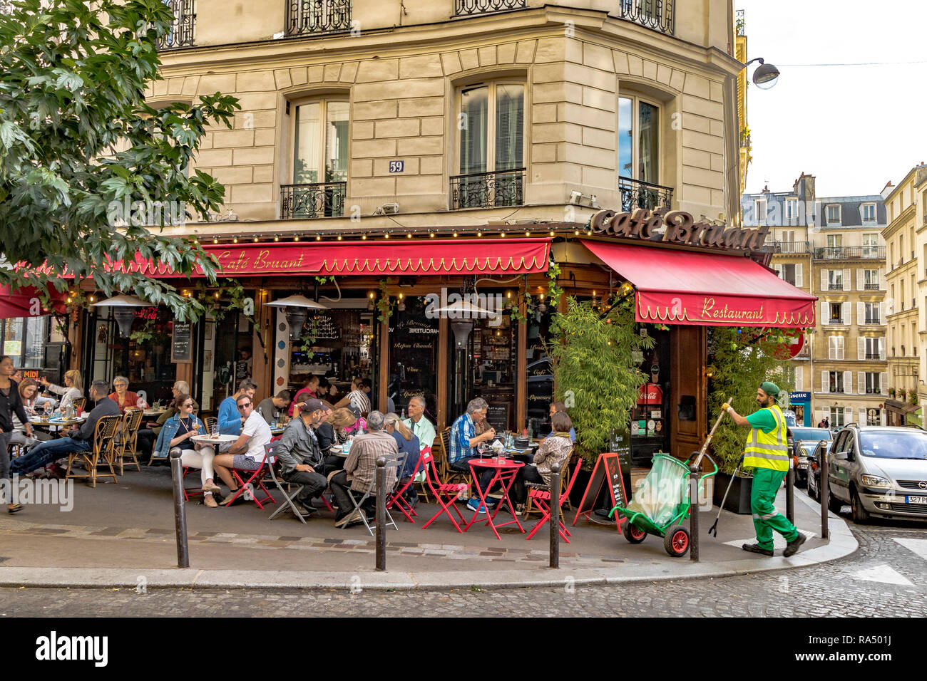 Les personnes mangeant le déjeuner dehors, sur le trottoir des tables à café Bruant restaurant et café,comme une balayeuse passe sur son travail, rue des Abbesses, Paris Banque D'Images