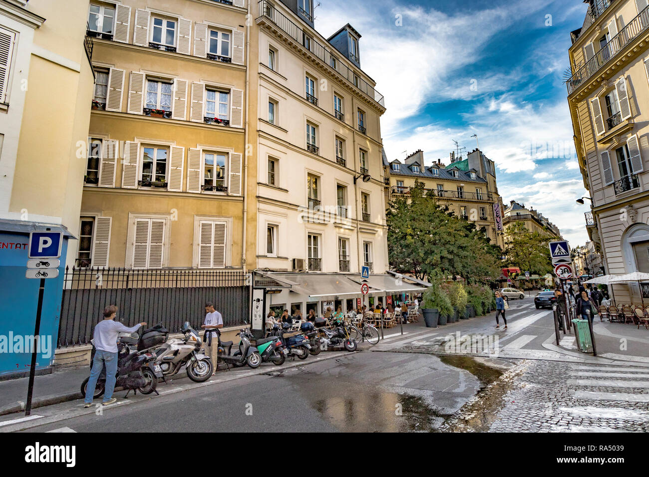 Un homme parcs nationaux un scooter à proximité d'un restaurant très fréquenté tandis qu'un autre homme regarde son téléphone, le long de la Rue de Douai dans ThePigalle,salon de Paris Banque D'Images