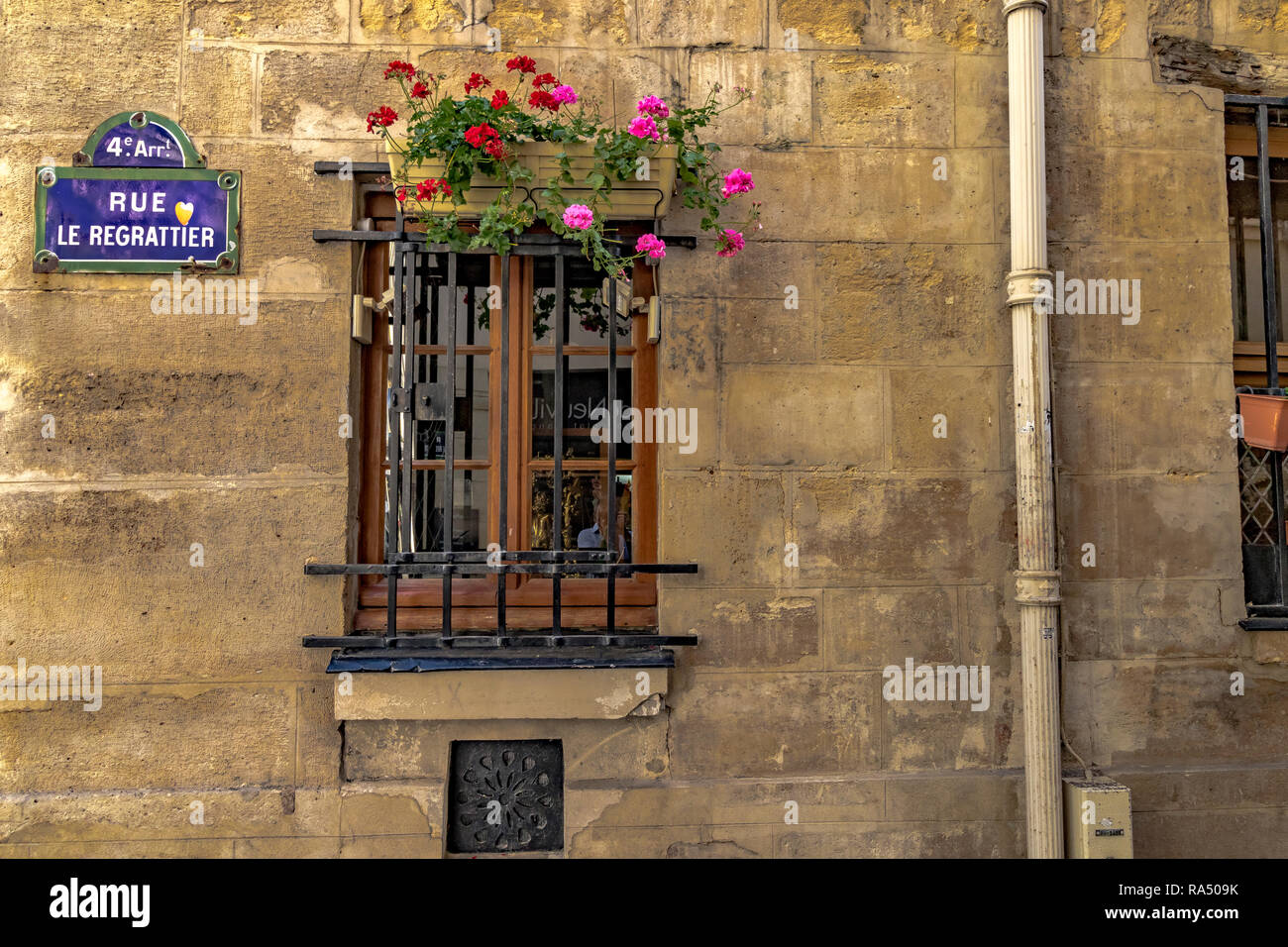 Une fenêtre en bois avec des barres de métal et une boîte à fleurs sur le dessus et un signe de la rue bleue sur un mur de pierre dans la rue Le Regrattier , l'Ile Saint-Louis, Paris Banque D'Images