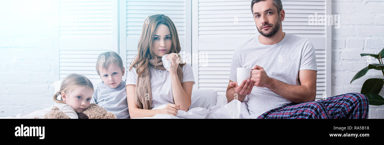 Vue panoramique de mari en donnant une tasse de thé à la femme malade, enfants looking at camera dans la chambre Banque D'Images