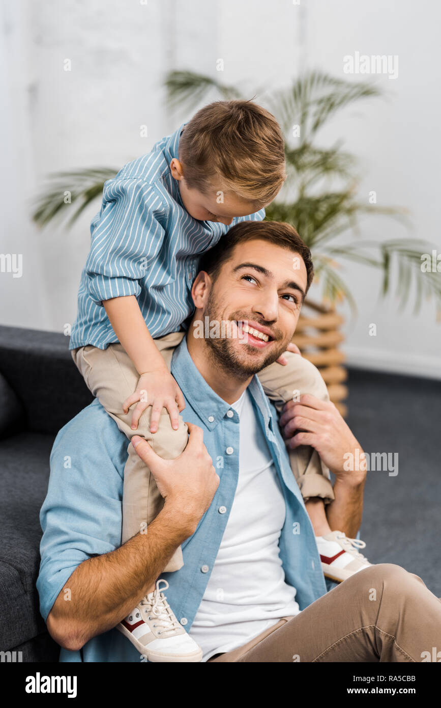 Smiling boy assis sur les épaules du père dans la salle de séjour Banque D'Images