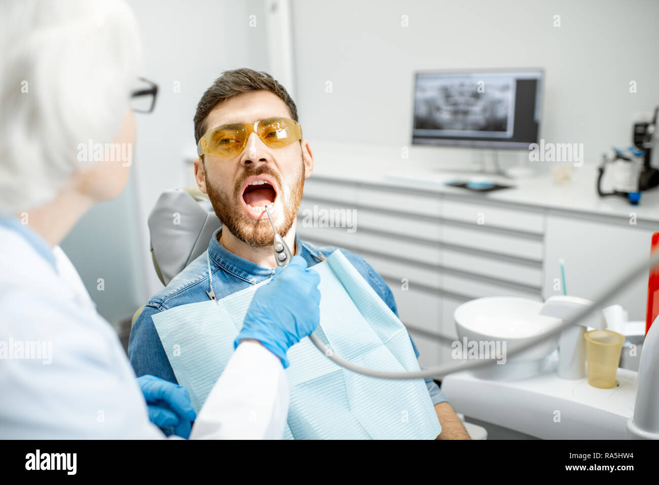 Bel homme lors de l'examen médical avec vieille femme dentiste dans le cabinet dentaire Banque D'Images