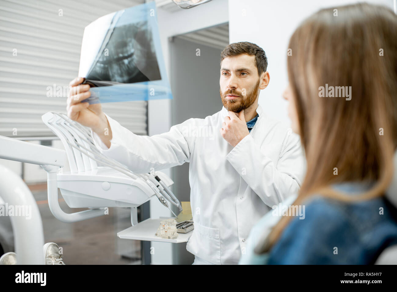 Beau dentiste contrôle radiographie panoramique d'une mâchoire durant la consultation médicale avec femme patient dans le cabinet dentaire Banque D'Images