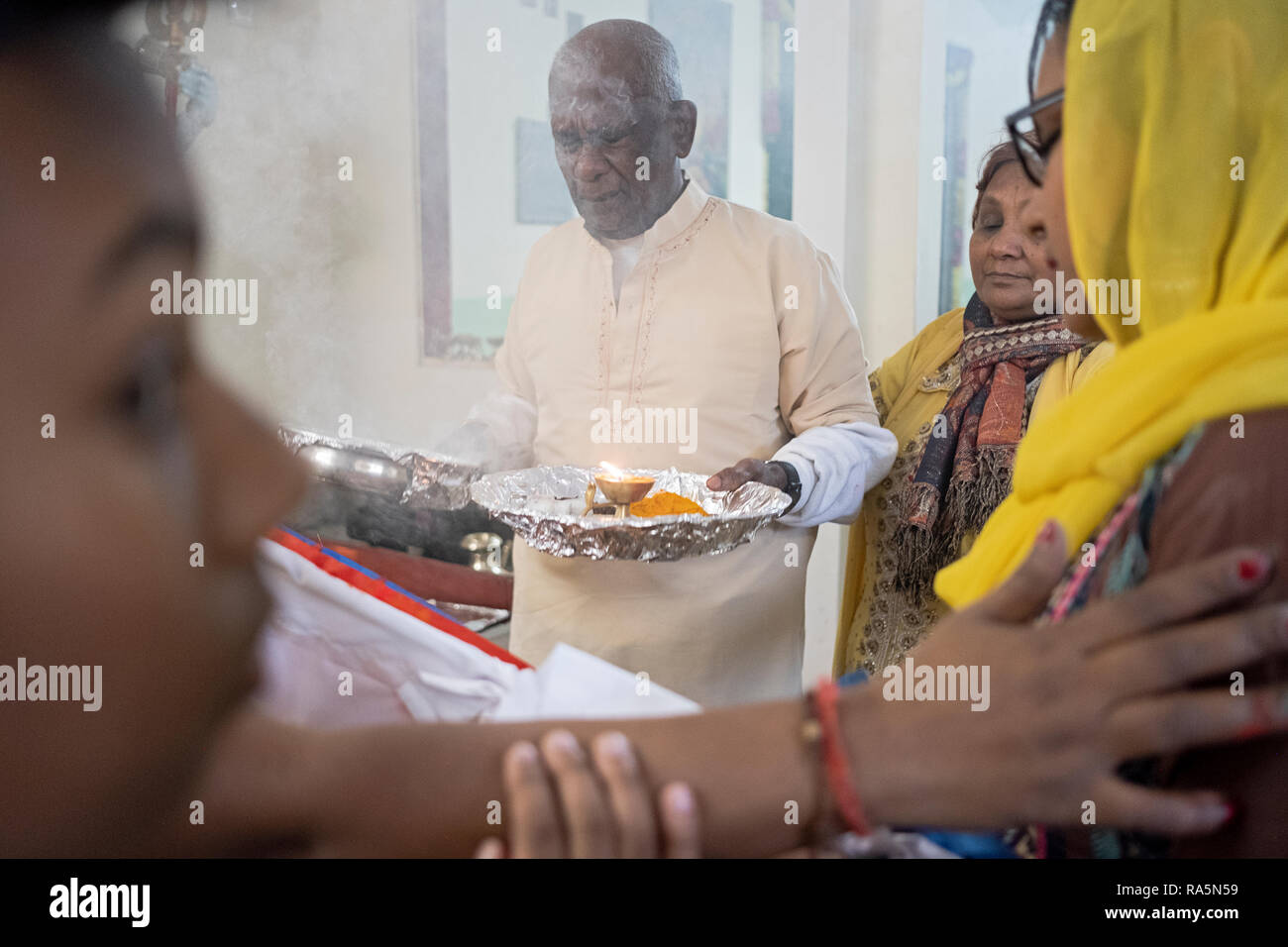 L'ARTI rituel. Un homme hindou dévot prie et vagues de feu devant les drapeaux de la victoire dans un temple dans le Queens, New York. Banque D'Images