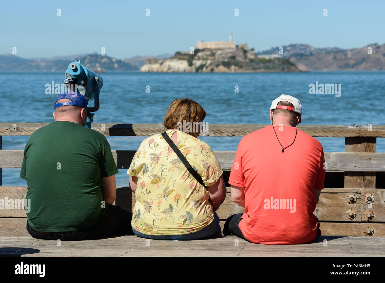 Les touristes assis sur un banc avec vue sur l'île et Alcatraz prison dans l'arrière-plan de Pier 39 à San Francisco Banque D'Images