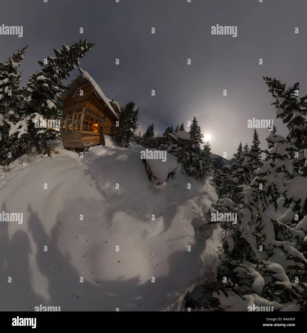 Vue aérienne chambre chalet durant une chute de neige dans les arbres forêt d'hiver la nuit au clair de lune Banque D'Images