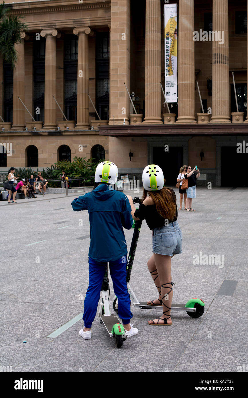 Les jeunes femmes sur la Chaux-S des scooters électriques par l'Hôtel de Ville, Brisbane, Queensland, Australie Banque D'Images