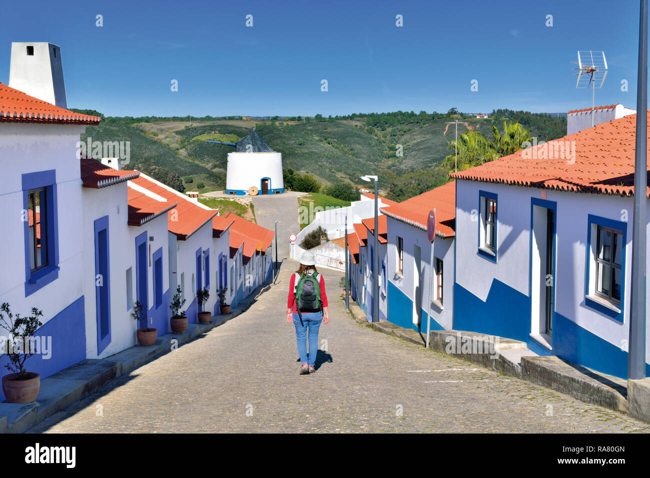 Woman walking along petite rue entre blanc, de maisons alignées avec ornements bleu Banque D'Images